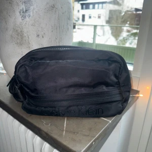 Svart necessär från Calvin Klein - Snygg svart necessär från Calvin Klein i slitstarkt tygmaterial. Praktisk dragkedja upptill och diskret logga framtill.