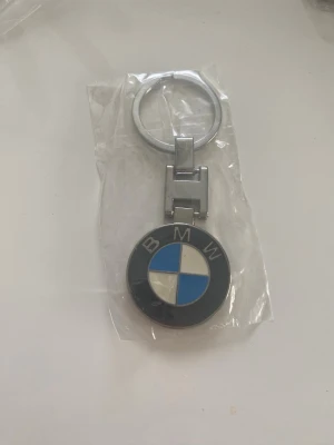 BMW nyckelring i metall - Snygg nyckelring med BMW:s klassiska logga i svart, vitt och blått. Tillverkad i metall med rund form och robust ring för nycklar. Perfekt accessoar för dig som gillar bilar och vill visa din stil.