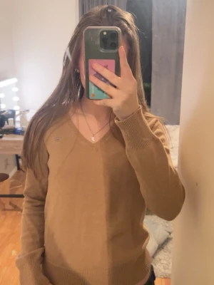 Brun v-ringad tröja från Gant - Säljer en brun v-ringad tröja från Gant med logga broderad på bröstet. Tröjan har långa ärmar och ribbade muddar vid ärmslut och nederkant. 