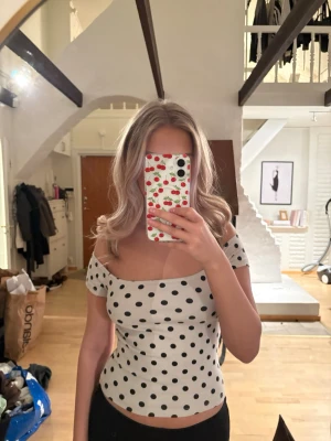 Vit prickig offshoulder topp - Vit topp med svarta prickar och offshoulder-design. Kortärmad.