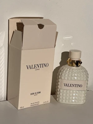 Valentino Uomo Born In Roma Ivory EdT - Exklusiv parfym från Valentino, Uomo Born In Roma Ivory, 100 ml. Flaskan är vit med ett coolt nitat mönster och gulddetaljer vid halsen. Kommer i matchande vit kartong med stilren design. Perfekt för dig som vill ha en unik och lyxig doft.