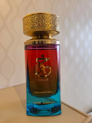 Khair Confection parfym Paris Corner - Unik parfymflaska från Paris Corner, modell Khair Confection. Flaskan har en snygg färgskiftning från rött till blått och är dekorerad med guldfärgade detaljer. Ny, endast använd 2 ggr, tyvärr utan kartong.  Toppnoter Päron, Grädde  Mellannoter Ylang ylang, Jasmin, kashmir  Basnoterna Vanilj, Marshmallow, Sandelträ, Marshmallow
