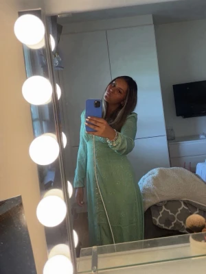 Ljusgrön långklänning från Adoore - Säljer en ljusgrön långklänning från Adoore med v-ringning och långa ärmar. Klänningen har små blommiga detaljer, knappar framtill och en lätt glansig yta. Perfekt för vår och sommar!