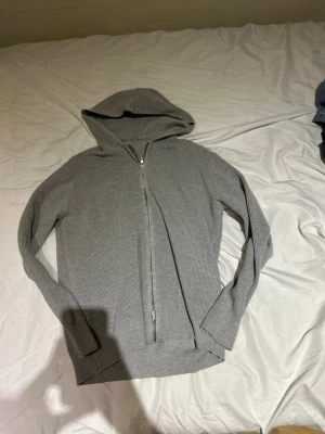 Grå zip hoodie i ribbat tyg - Säljer en stilren grå hoodie med dragkedja framtill och huva. Hoodien är tillverkad i ett ribbat material som ger en skön och avslappnad känsla. Perfekt för dig som gillar en enkel men snygg look.