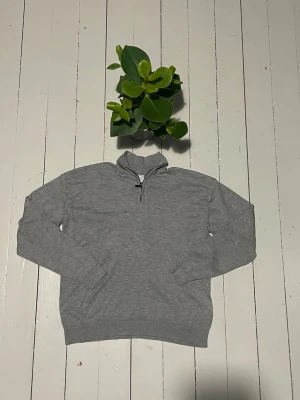 Grå halvzip sweatshirt - En stilren grå sweatshirt med halv dragkedja och hög krage. Tröjan har långa ärmar, ribbade muddar och är tillverkad i mjukt bomullsmaterial. Perfekt för en avslappnad och trendig look. Storleken på denna tröja är 146/152 men den har krympt en del i tvätten så kolla gärna måtten nedan.                                             Axelbredden är 46cm, längden är 52cm och ärmarna är 52cm. Tröjan har även några hål i ena armhålan men jag tror att det lätt går att sy ihop