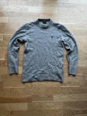 Grå stickad tröja  - Klassisk grå stickad tröja med rund halsringning och ribbade muddar. Tröjan har en diskret broderad logotyp på bröstet och är tillverkad i mjukt material som passar perfekt till lager på lager-stil. Märket är next signature.