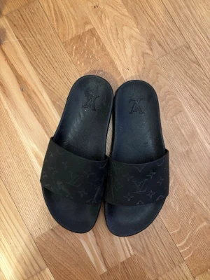 Svarta Louis Vuitton sandaler - Säljer dessa LV tofflor. Dom är skjöld med vatten på bilderna men kan självklart tvätta dom noggrannare vid köp! Osäker på om dom är äkta, men relativt bra skick ändå! Kantern har lite märken så priset kan diskuteras!
