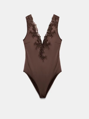 Brun spetsbody med djup V-ringning - Snygg brun body med djup V-ringning och dekorativa spetsdetaljer framtill. Tillverkad i ett glansigt, stretchigt material som sitter tight mot kroppen. Perfekt att styla under kavaj eller till höga byxor för en trendig look.