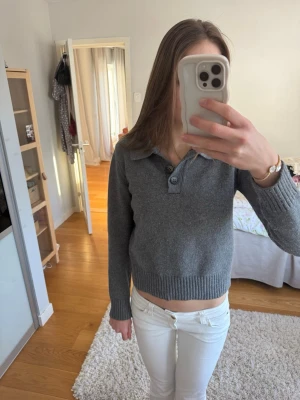 Grå stickad tröja med krage från Zara - Mysig grå stickad tröja från Zara med klassisk krage och tre knappar framtill. Tröjan har långa ärmar och breda ribbstickade muddar vid ärmslut och nederkant. Perfekt för lager-på-lager och enkel att matcha.