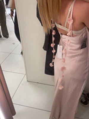 Ljusrosa långklänning i satin - Säljer en elegant ljusrosa långklänning i satin med smala axelband och dekorativa rosetter. Klänningen har en mjuk, glansig yta och en figurnära passform som ger en snygg siluett. Perfekt för dig som vill ha en stilren och trendig look. Den har inga defekter❤️