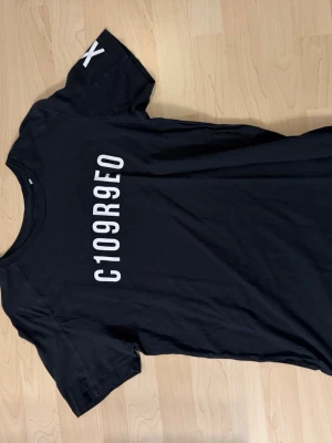 Svart t-shirt med tryck C109R9EO - Svart t-shirt med vitt tryck C109R9EO på framsidan och ett X på ärmen. Klassisk rund hals och korta ärmar. Perfekt för en avslappnad och cool stil.