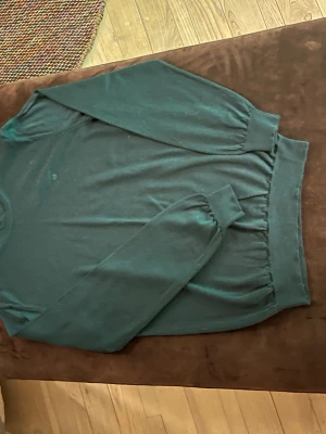 Mörkgrön merinoullströja från Gant - Mörkgrön stickad tröja från Gant i fin merinoull. Tröjan har rund halsringning, långa ärmar och ribbade muddar vid ärmslut och nederkant. Perfekt för dig som gillar klassisk och stilren design.