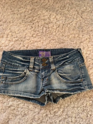 Blå lågmidjade  jeansshorts från Bershka  - Säljer ett par blå denimshorts från Bershka med slitna detaljer och dubbla knappar framtill. Shortsen har klassiska fem fickor och coolt leopardmönstrat innerfoder. 