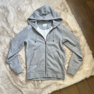 Grå hoodie med dragkedja från Jack&Jones - Säljer en stilren grå hoodie från Jack&jones med hel dragkedja och huva med snörning, Ny skick. Xs men sitter som S