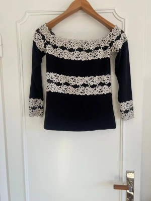 Svart offshoulder topp med spets från Intimissimi som inte säljs längre🥰 - Snygg svart offshoulder topp med vita spetsdetaljer över bröst, ärmar och midja. Toppen har lång ärm och sitter tight. Perfekt för dig som vill ha en unik och elegant look. 💕💕