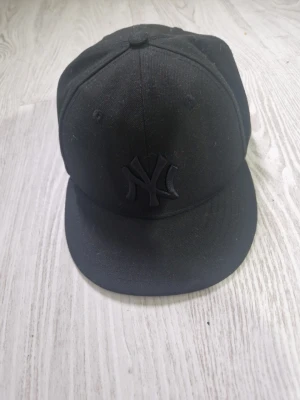 Svart New Era Yankees keps - Snygg svart keps från New Era med New York Yankees-logga broderad framtill i samma färg som kepsen. Klassisk rak skärm och sex paneler. Tillverkad i bomullsmix för en bekväm passform. Perfekt för dig som vill ha en stilren och sportig look.
