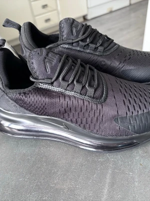 Nike Air Max 720 helsvarta sneakers - Snygga helsvarta Nike Air Max 720 sneakers med mesh- och syntetmaterial, tydlig Air Max-sula och diskreta loggor. Skorna har rundad tå, svarta skosnören och ventilerande ovandel. Perfekta för dig som gillar sportig och modern stil.