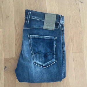 Blå Replay Hyperflex jeans - Säljer ett par blå Replay Hyperflex jeans med snygg tvätt och klassisk femficksmodell. Jeansen har en slim fit passform och är tillverkade i stretchigt material för extra komfort. Märkespatch bak i midjan och slitningar för en trendig look.
