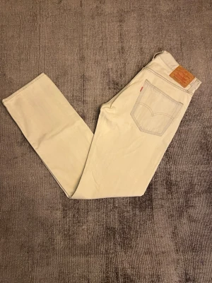 Ljusbeiga raka jeans från Levi's - Säljer ett par ljusbeiga jeans från Levi's med klassisk rak passform. Jeansen har Levi's ikoniska läderpatch bak i midjan och röda etikett på bakfickan. Bra skick på byxorna med ändas ett litet hål mellanbenen som kan lätt sys ihop     (kolla sista bilden)