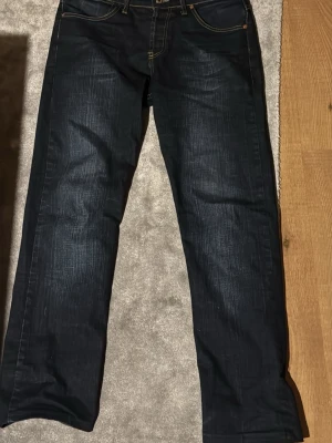 Mörkblå raka jeans från Levi's - Säljer ett par mörkblå jeans från Levi's med raka ben och klassiska kontrastsömmar. Jeansen har fem fickor och Levi's ikoniska bakfickor med bågformad söm. Materialet är kraftig denim i bomull. Perfekta för en avslappnad och tidlös stil.