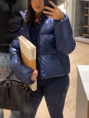 Mörkblå pufferjacka med hög krage - Snygg mörkblå pufferjacka med   glansig finish. Jackan har en boxig passform och dragkedja framtill. Perfekt för kalla dagar när du vill hålla värmen och ändå se trendig ut.