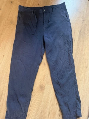Mörkblå linnebyxor från Zara - Snygga mörkblå linnebyxor med avslappnad passform och dragsko i midjan. Byxorna har knapp och gylf framtill samt sidofickor. Perfekta för en chill och stilren look. Materialet är luftigt linne som ger en skön känsla. Pris kan diskuteras.