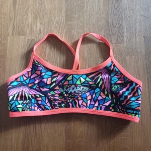 Färgglad sport bikini från Amanzi - Säljer en sportbikini från Amanzi med färgstarkt geometriskt mönster i lila, blått, grönt och rosa. Bikinin har smala axelband, perfekt för träning eller en solig dag på stranden.