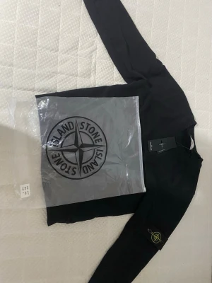 Svart sweatshirt från Stone Island - Snygg svart sweatshirt från Stone Island med den klassiska logotypen på ärmen. Tröjan har rund halsringning och långa ärmar. Perfekt för dig som gillar streetwear och vill ha en stilren look.