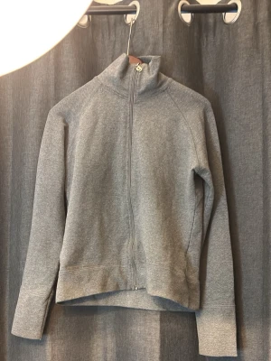 Grå hoodie med dragkedja - Säljer en stilren grå hoodie med hel dragkedja och hög krage. Hoodien har långa ärmar och är tillverkad i mjukt sweatshirtmaterial. Perfekt för en avslappnad look och enkel att matcha med andra plagg.