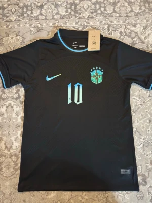 Svart Brasilien fotbollströja Nike - Snygg svart fotbollströja från Nike med Brasilien-emblem och nummer 10 i blått på framsidan. Tröjan har texten 'Free Kurdistan' och nummer 10 på ryggen. Tillverkad i ett lätt och ventilerande material, perfekt för träning eller match.