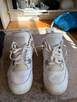 Vita Air Jordan 4 pure money sneakers - Säljer ett par vita Air Jordan 4 Retro sneakers med klassisk mesh och läderdetaljer. Skorna har ikoniska plastdetaljer vid snörningen och synlig Air-sula. Perfekta för dig som gillar streetwear och vill ha en clean look.