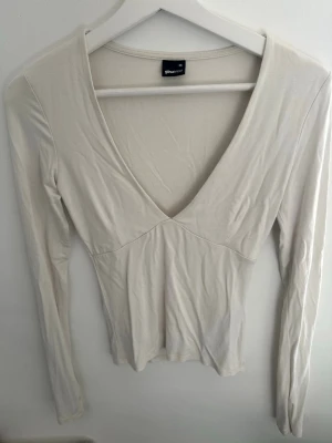 Vit v-ringad långärmad topp - Säljer en stilren vit långärmad topp från Gina Tricot med djup v-ringning. Toppen har en figurnära passform och är tillverkad i mjukt, stretchigt material som känns skönt mot huden. Perfekt att matcha med jeans eller kjol.