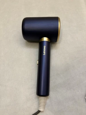 Lenovo hårfön blå och guld - Säljer en stilren hårfön från Lenovo i mörkblått med gulddetaljer. Hårfönen har en modern, cylinderformad design och levereras med ett avtagbart munstycke. Sladden är svart och handtaget har en knapp på sidan.