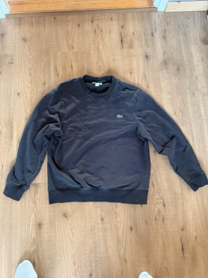 Mörkgrå sweatshirt från Lacoste - Klassisk mörkgrå sweatshirt från Lacoste med rund halsringning och den ikoniska krokodilloggan broderad på bröstet. Tröjan har långa ärmar. Perfekt för en avslappnad och stilren look. Pris kan diskuteras. 