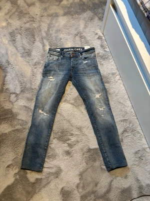 Slim fit jeans från Jack & Jones - Snygga blå slim fit jeans från Jack & Jones, modell Glenn. Jeansen har slitna detaljer och klassisk femficksdesign. Perfekta för en avslappnad och trendig look. Tillverkade i denim med stretch för extra komfort.