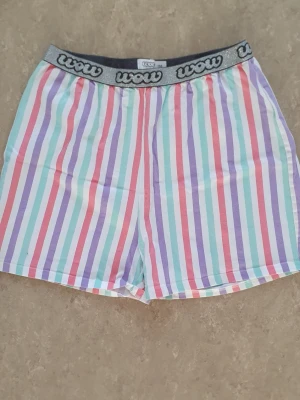 Shorts - Färgglada shorts från Wow med vertikala ränder i lila, mintgrön, röd och vit. Shortsen har en bred resår i midjan med Wow-logga och är tillverkade i mjuk bomull. Perfekta för sommarens alla dagar.