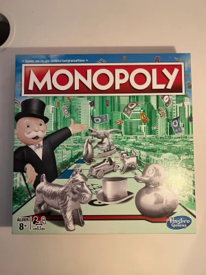 Monopol brädspel från Hasbro - Säljer det klassiska brädspelet Monopol från Hasbro Gaming. Spelet innehåller spelplan, spelpjäser i metall, kort, pengar och tärningar. Perfekt för 2-8 spelare och rekommenderas från 8 år. Lådan har färgglad design med stadsmotiv och ikoniska Monopol-symboler.