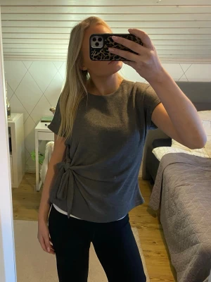 Grå topp med knyt från Zara - Säljer en grå topp från Zara med korta ärmar och rund halsringning. Toppen har en snygg knytdetalj i sidan som ger en unik look. Materialet känns mjukt och stretchigt, perfekt för en chill och stilren outfit.