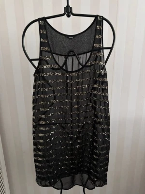 Svart glittrig linnetopp/strandtunika  från mbyM  - Säljer en svart ärmlös linnetopp eller strandtunika  från mbyM med glittriga horisontella ränder. Toppen är transparent och har en loose passform, perfekt för att sticka ut. Materialet känns lätt och luftigt, och toppen har en rund halsringning.