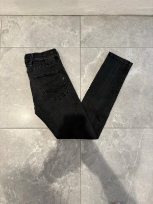  Replay Anbass  - Snygga svarta slim fit jeans från Replay med klassisk femficksdesign och diskret logga på myntfickan. Jeansen har en något tvättad look och är tillverkade i stretchigt denim för extra komfort. Perfekta för dig som gillar en stilren och modern vibe.