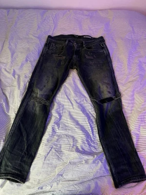 Replay mörk blåa slitna jeans med hål - Säljer ett par svarta jeans med slitningar och hål på knäna. Jeansen har klassisk femficksdesign och är tillverkade i denim. Perfekt för dig som gillar en edgy och avslappnad stil.
