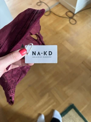 Vinröd spetskorsett från NA-KD - Säljer en snygg vinröd korsett från NA-KD med breda axelband och spetsdetaljer. Modellen har hakknäppning framtill och är tillverkad i ett mjukt, stretchigt material som formar sig efter kroppen. Perfekt för dig som vill ha något extra till outfiten.