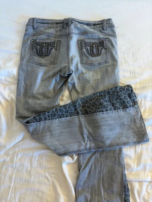 Unika vintage low waist jeans (grå med leoparddetaljer) - Säljer ett par helt unika egensydda jeans  Gråa low waist bootcut jeans med sjukt coola leoparddetaljer som verkligen sticker ut. Fickorna är en riktig statement-detalj och gör hela plagget extra unikt 🐆✨  Jeansen har en vintage vibe och sitter lågmidjat för en trendig Y2K-look. Sömmarna är inte helt perfekta, vilket ger en rå och edgy känsla – perfekt om du gillar plagg med karaktär 💥  • Unika och vintage • Färg: Grå med leoparddetaljer • Lågmidjade (low waist) och utsvängda (bootcut) • Small