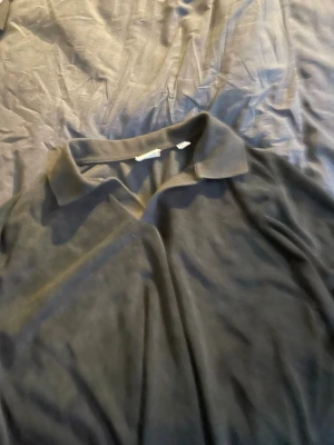 Svart pikétröja med krage - Klassisk svart pikétröja med krage och kort ärm. Enkel och stilren design som passar till det mesta. Tillverkad i mjukt material för en bekväm känsla. Perfekt för dig som gillar en clean och tidlös look.