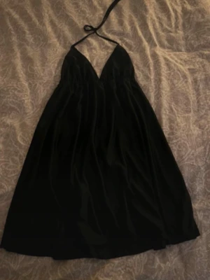 Svart halterneckklänning BikBok - Snygg svart klänning från BikBok med halterneck och v-ringad urringning. Klänningen har en luftig passform och är tillverkad i ett glansigt material som ger en elegant look. Perfekt för dig som vill sticka ut med en enkel men stilren outfit.