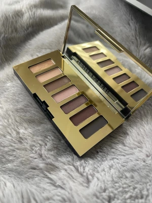 Estée Lauder ögonskuggspalett nude - Snygg ögonskuggspalett från Estée Lauder med sex nyanser i nude och bruna toner. Paletten har ett elegant guldfärgat fodral med räfflad yta och spegel på insidan. Perfekt för att skapa naturliga och smokey looks.