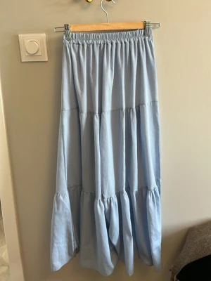 Ljusblå långkjol   - Säljer en lång, ljusblå kjol med volangdetaljer och resår i midjan. Kjolen har en luftig och flowy passform, perfekt för varma dagar. 