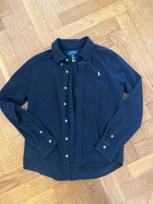Mörkblå skjorta från Polo Ralph Lauren - Klassisk mörkblå skjorta från Polo Ralph Lauren med vit logga på bröstet. Tillverkad i mjuk bomull.