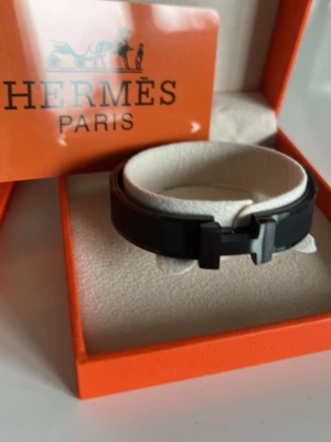 Svart armband i stål - Snyggt svart armband från i läder med den ikoniska H-detaljen framtill. Kommer i original ask och påse, perfekt för dig som gillar exklusiva accessoarer med stilren design. Passar till många olika looks och är lätt att matcha.