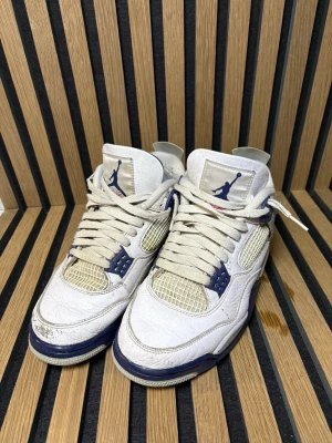 Air Jordan 4 mid night navy - Säljer ett par vita Air Jordan 4 Retro sneakers med blå detaljer och meshpaneler på sidorna. Skorna har den klassiska Jumpman-loggan på plösen och häl, samt synlig Air-dämpning i sulan. Ovandelen är i läder och mesh, och sulan har stänk av blått. Kommer med box!!!